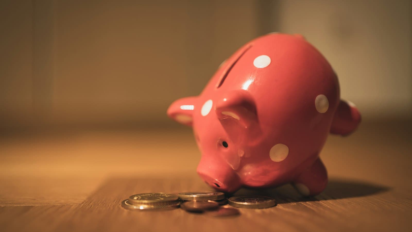 Tirelire rose posée sur une table en bois à côté de pièces de monnaie
